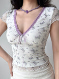 Front view of a woman wearing a white mesh top with a purple floral print. The V-neckline is trimmed with purple lace, and a purple ribbon is tied at the center.