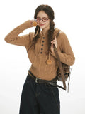 Woman in a brown hooded cable knit sweater, playing with drawstring pom-pom