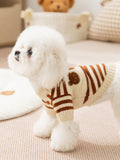 A small white dog in profile wearing a cream and brown striped knit sweater with a crew neck and short sleeves.