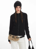 Close-up of a woman wearing a black zip-up fleece jacket, white pants, and a black beanie.