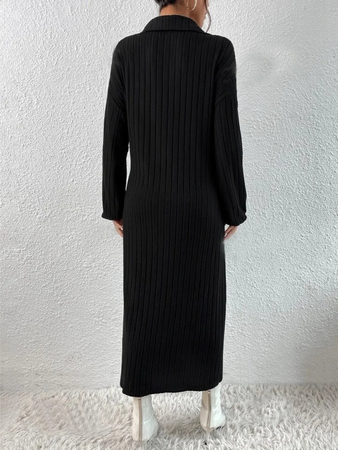 Model wearing a black ribbed knit midi dress with a pointed collar and v-neck, featuring long sleeves and a side slit.