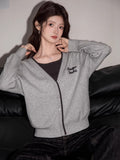 Woman wearing a grey V-neck knit cardigan with contrast trim and embroidered graphic detail