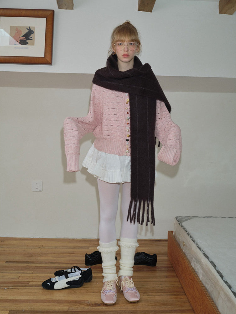 Full body shot of a woman in a pink cardigan, white skirt, and dark brown scarf.