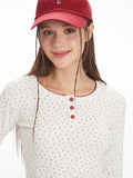 Front view close-up of a woman smiling, wearing a white long-sleeve top with a red floral print and red trim.