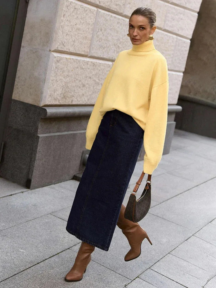 Woman wearing an orange oversized turtleneck sweater, dark brown wide-leg trousers, and holding a dark handbag.