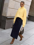 Woman wearing an orange oversized turtleneck sweater, dark brown wide-leg trousers, and holding a dark handbag.