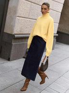 Woman wearing an orange oversized turtleneck sweater, dark brown wide-leg trousers, and holding a dark handbag.