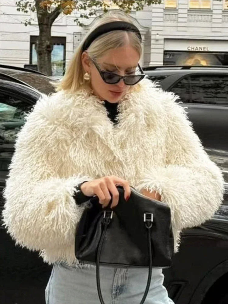 Woman wearing a white shaggy faux fur cropped jacket and light blue jeans, holding a coffee cup.