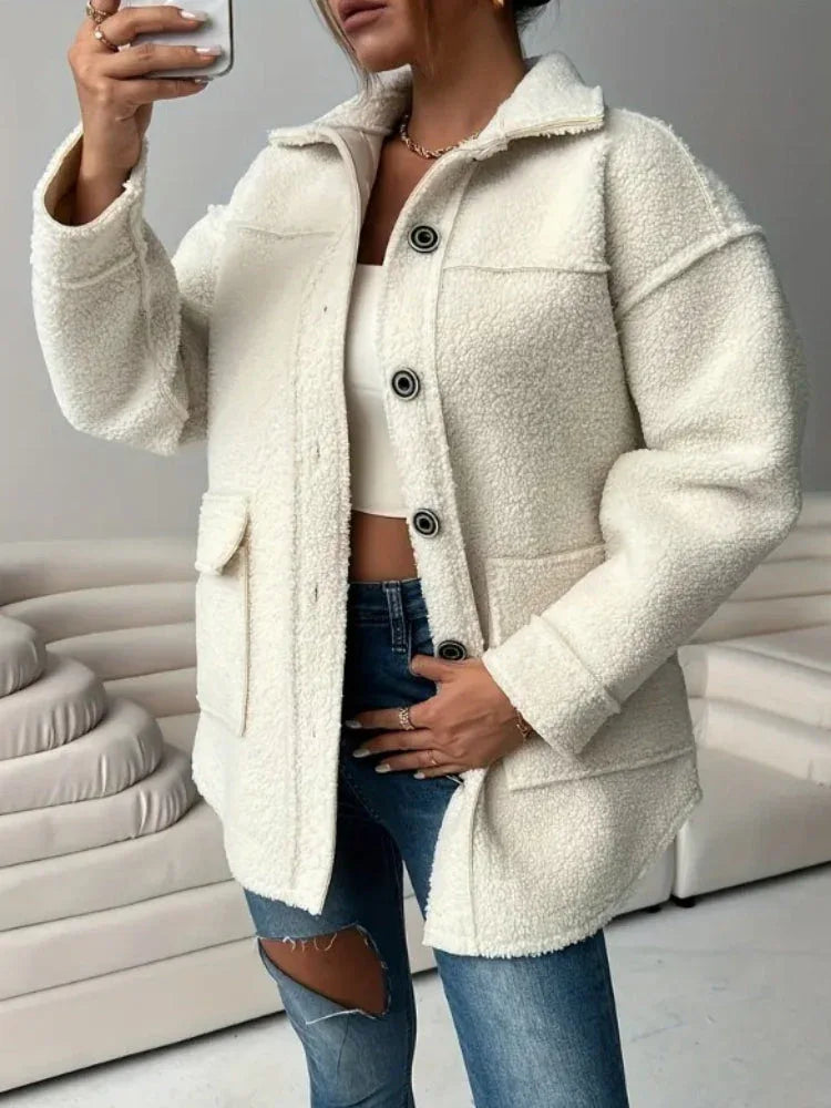 Woman holding her phone and wearing a cream-colored oversized fleece jacket, styled with blue jeans.
