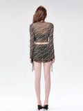 Back view of a woman in a sheer striped long-sleeve crop top and mini skirt