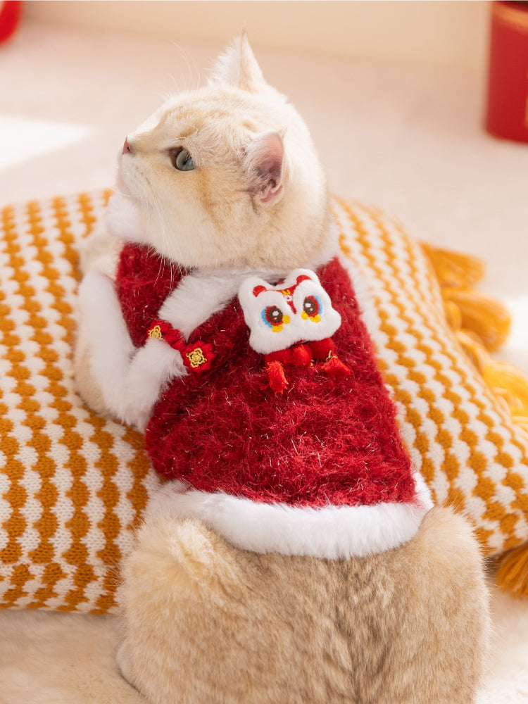 Close-up of a cat wearing a festive red vest with a white embroidered lion head applique and red tassels.