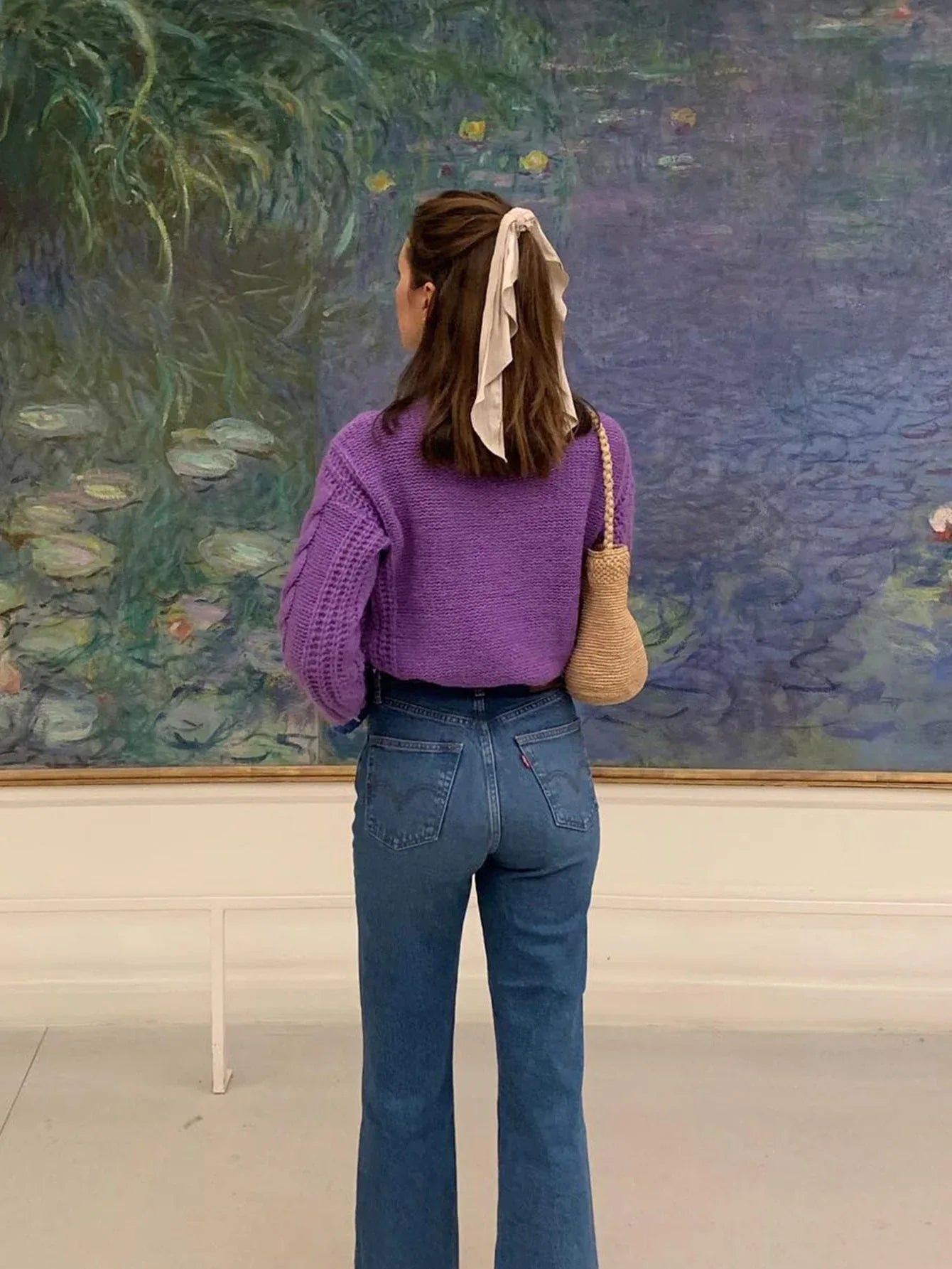 Rear view of a woman wearing a purple cable knit cardigan and blue denim jeans.