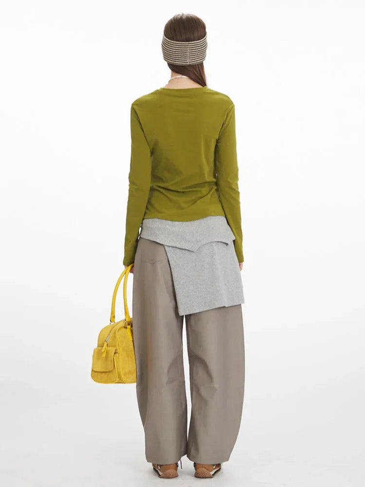 Rear view of a model wearing a long-sleeve olive green top with ruched side detail, grey layered vest, and taupe wide-leg pants.