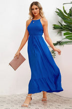 Woman in a royal blue smocked halter maxi dress with a tiered ruffle hem, holding a pink clutch.