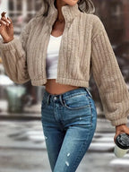 Woman in a tan fuzzy fleece cropped bomber jacket and blue jeans, holding a coffee cup.