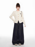 Full-body shot of a woman in a cream cable knit cardigan and dark wide-leg jeans, showcasing the garment's fitted silhouette and casual styling.