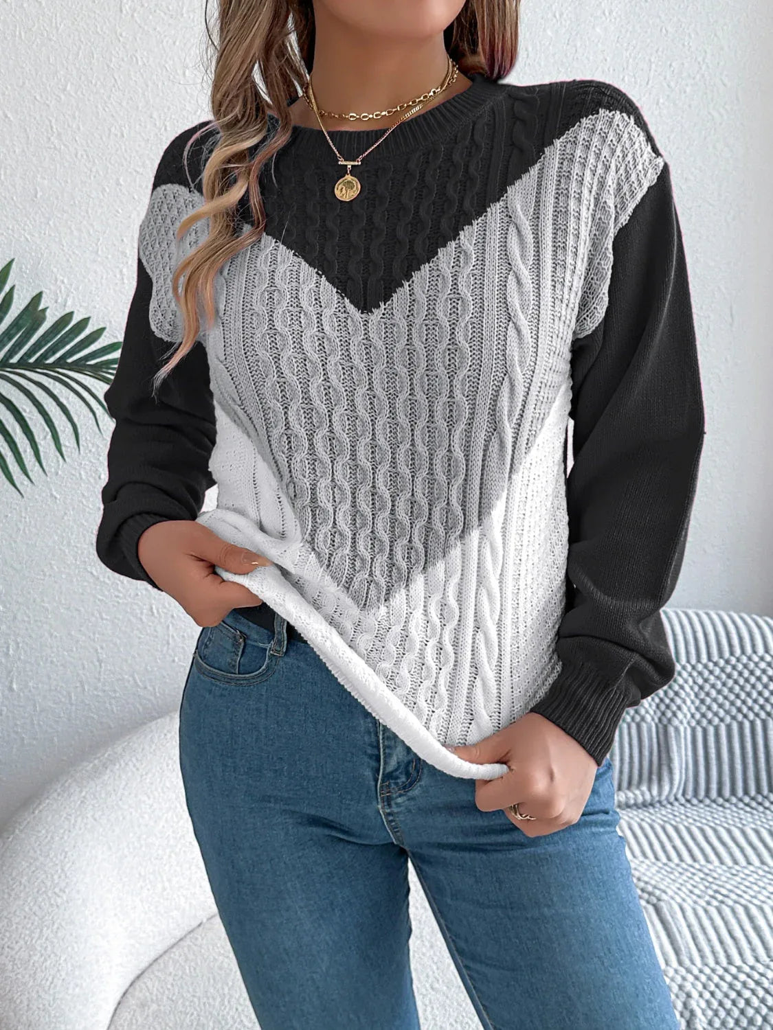 Woman wearing a black, grey, and white chevron color block cable knit sweater with blue jeans. Main image