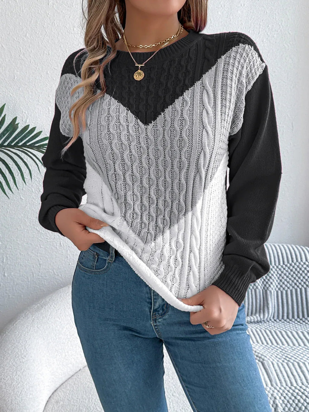 Woman wearing a black, grey, and white chevron color block cable knit sweater with blue jeans.