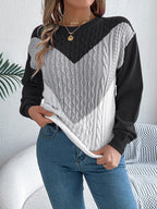 Woman wearing a black, grey, and white chevron color block cable knit sweater with blue jeans.