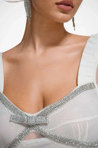 Close-up of the neckline of a white gown featuring a bow detail and sparkling embellishments