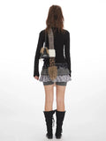 Back view of a woman wearing a black long-sleeve top, layered skirt, scarf, and boots