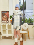 Woman wearing a light blue knit beanie, a large white and blue striped knit scarf with fringe, a grey knit sweater with a diamond pattern, white gloves, and white knee-high socks.