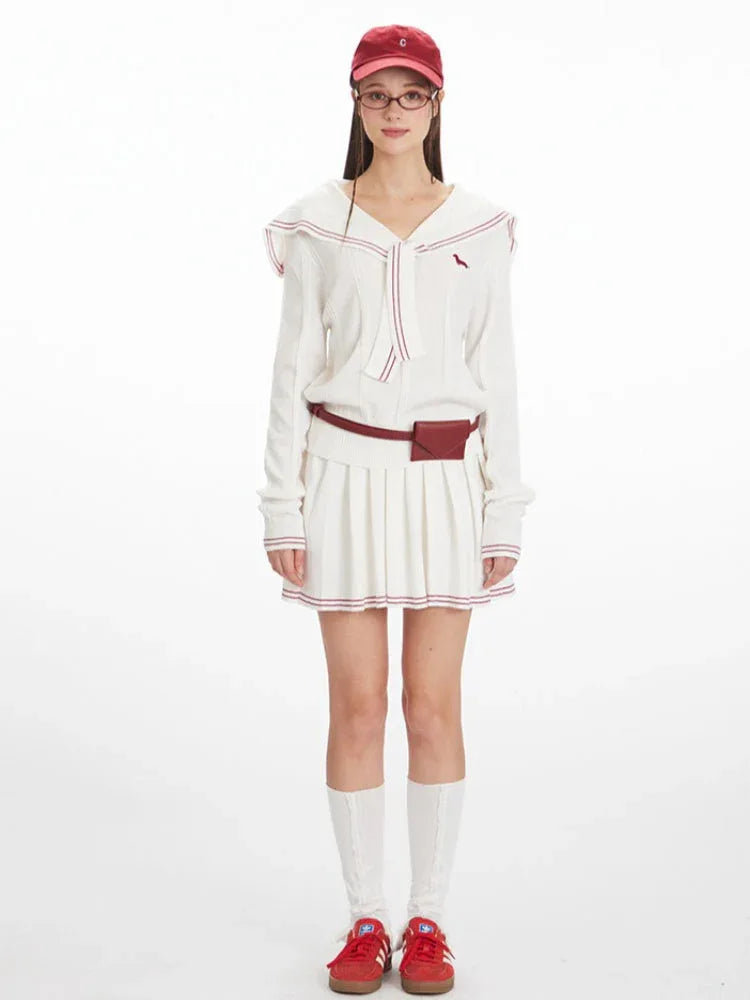 Woman wearing a white knit sweater with a navy sailor collar and red trim, paired with a white pleated skirt.