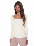 Woman wearing a fitted, long-sleeve cream ribbed top with a scoop neckline.