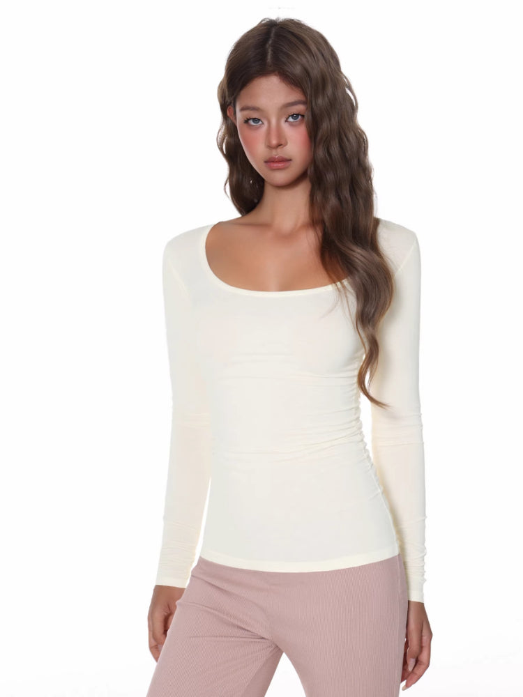 Woman wearing a fitted, long-sleeve cream ribbed top with a scoop neckline.