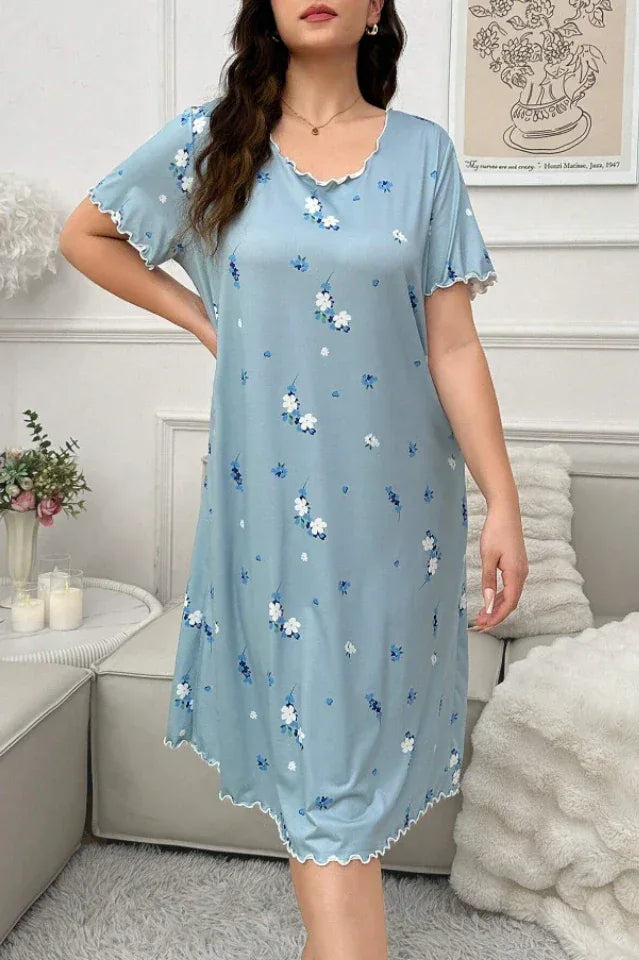 Woman in a light blue floral print nightgown posing while seated on a sofa.