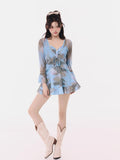 Woman wearing a blue abstract print sheer overlay dress with ruffled neckline and tie front