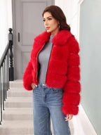 Woman standing, modeling a red faux fur jacket with a zipper down the front and a relaxed fit.