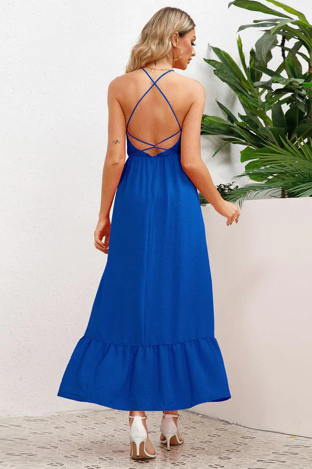 Back view of a woman in a royal blue smocked halter maxi dress with a tiered ruffle hem and crisscross back straps.