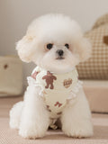 A Bichon Frise dog wears a light yellow padded vest with a teddy bear print and white ruffle trim.