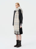Woman wearing a plaid scarf with blue and beige squares and a fringed hem, paired with a black jacket and black skirt.