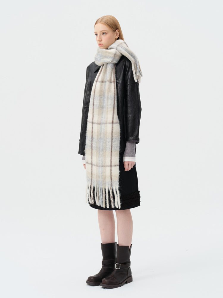 Woman wearing a plaid scarf with blue and beige squares and a fringed hem, paired with a black jacket and black skirt.