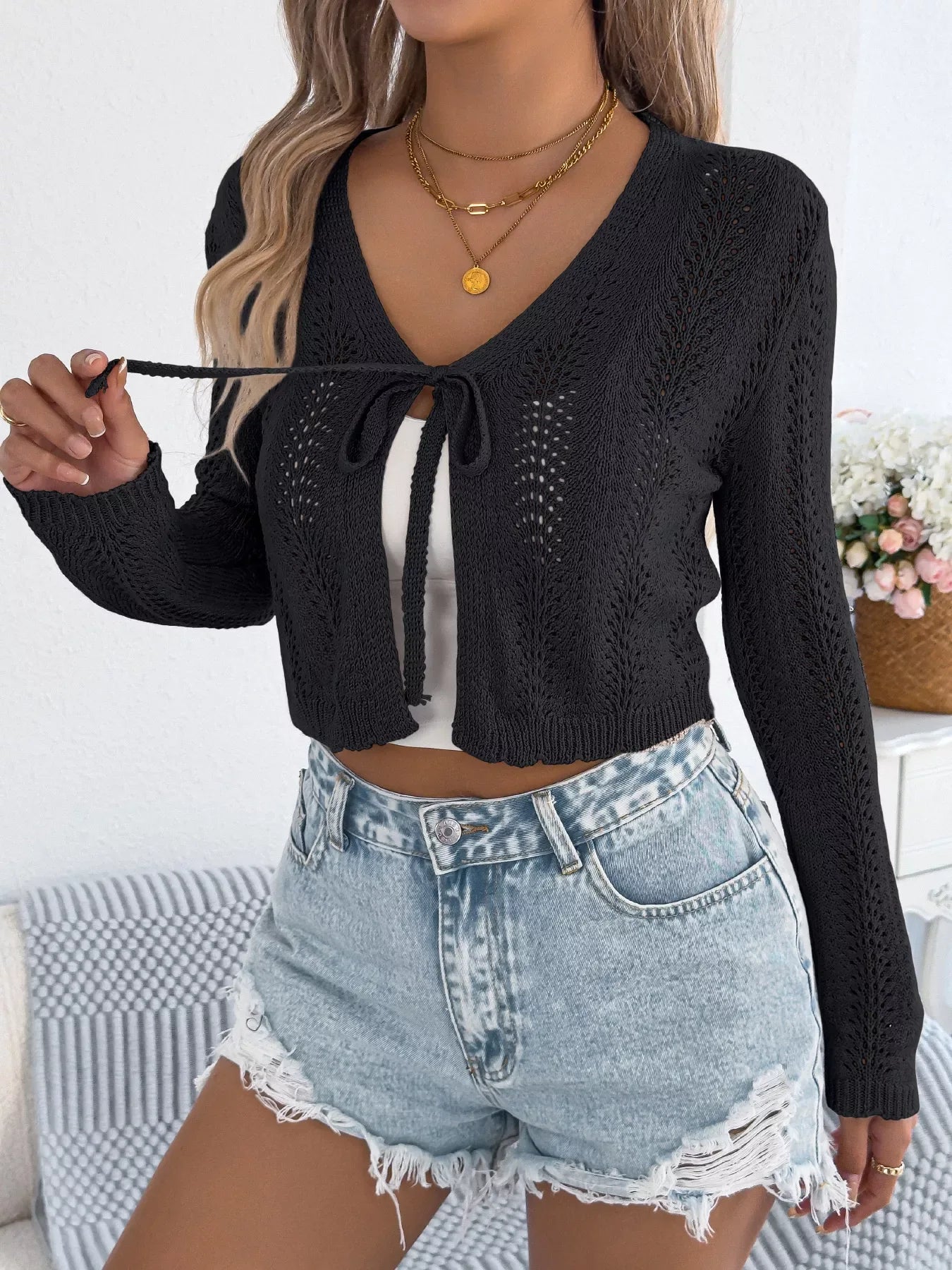 Close-up of a woman adjusting the tie on her black knit cardigan.
