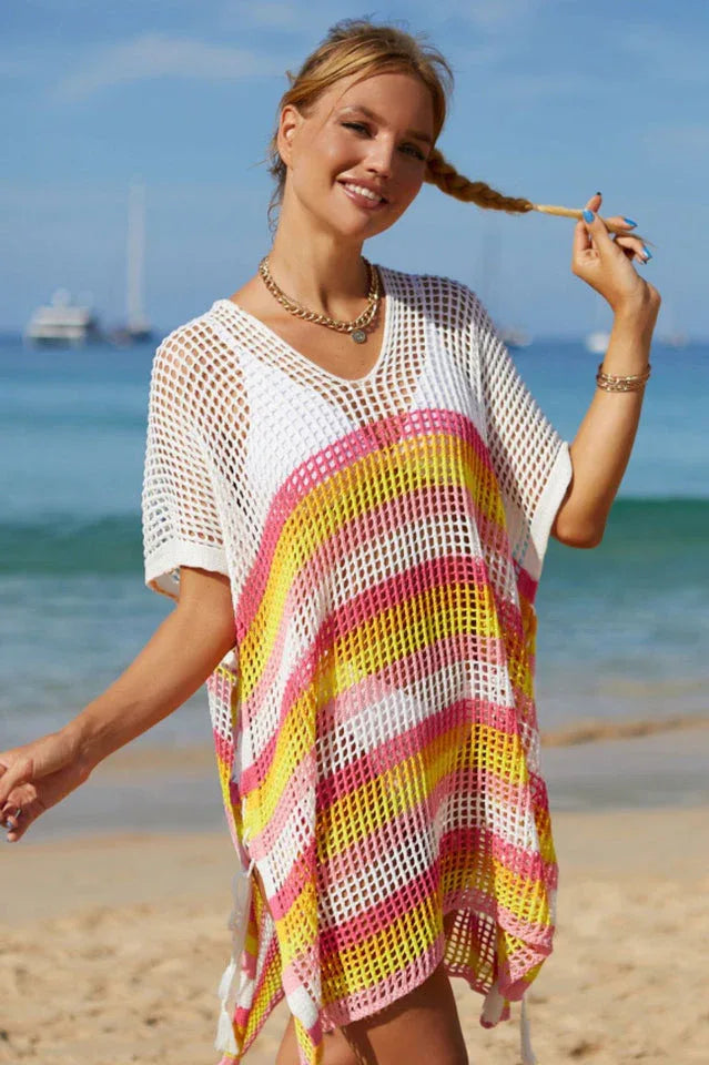 Woman with braided hair, wearing a white and striped mesh knit tunic on a beach.