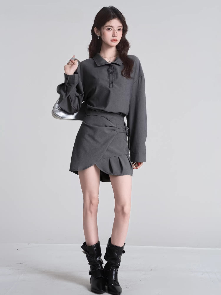 Woman posing in a grey collared shirt and skirt outfit with boots