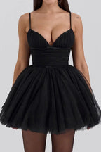Woman wearing a short black tulle dress with ruched bodice and spaghetti straps.
