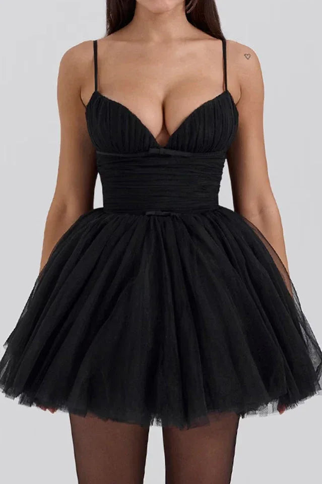 Woman wearing a short black tulle dress with ruched bodice and spaghetti straps.