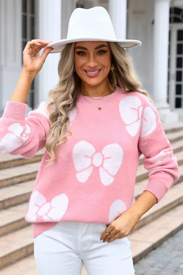 Woman wearing a pink knit sweater with white bow print and a white hat.
