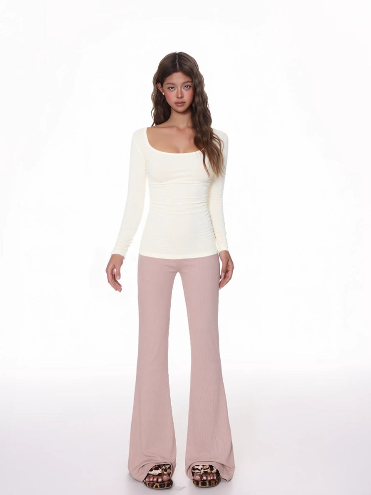 Full body shot of a woman wearing a cream ribbed long-sleeve top and pink flared pants.