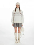 Woman wearing a white Fair Isle half zip knit sweater with a snowflake pattern and a heart zipper pull.
