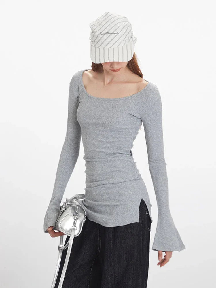 Close-up front view of a woman wearing a grey long-sleeved ribbed knit top with a scoop neckline, ruched side detail, and flared cuffs.