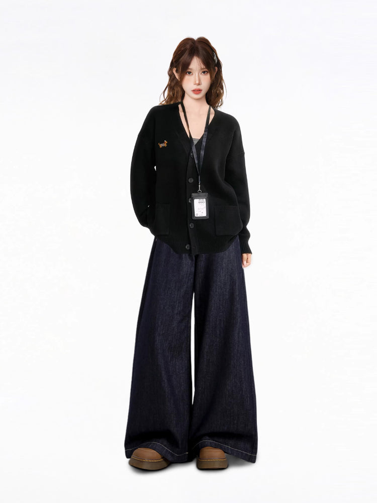Woman wearing a black oversized knit cardigan with a V-neck, button-down front, and dual front pockets. The cardigan features an embroidered dachshund graphic on the left chest.