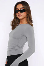 Side view of a woman in a grey long sleeve cropped top with ruched sides