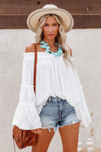 Woman wearing a white off-the-shoulder blouse with bell sleeves and denim shorts.