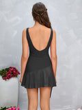 Woman from behind wearing a black sleeveless square neck fit and flare dress with ruched bodice and asymmetrical chiffon overlay skirt