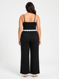 Back view of a woman in a black plus-size pajama jumpsuit with wide legs and white lace trim.
